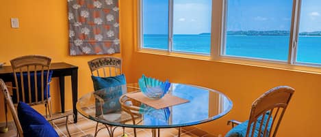 A dining area with a glass table and chairs, a view of the sea, and a wall with a coral pattern.