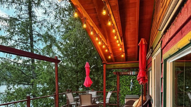 Een houten terras met rieten meubilair, rode parasols en lichtslingers.