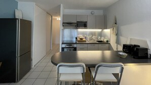 A compact kitchen with a refrigerator, microwave, oven, and a dining area with two chairs.