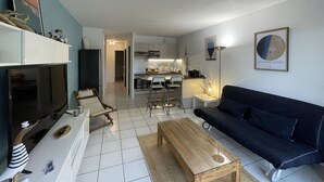 A modern living room with a TV, sofa, coffee table, and a kitchen in the background.