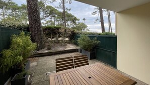 A patio with a wooden table and benches, surrounded by a green fence, trees, and a pergola.