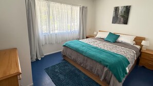 Une chambre avec un grand lit, une fenêtre avec des rideaux, une table de chevet avec une lampe et un tableau au mur.
