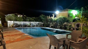 A swimming pool with a tiled deck, surrounded by outdoor furniture and plants.