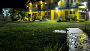 A multi-story yellow building with a well-lit entrance and a paved pathway leading to the door.