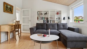 A modern living room with a grey sectional sofa, a round white coffee table, a wooden desk with a chair, and a bookshelf filled with books and decorative items. - "Dreng" - 250m from the sea by Interhome (Nexø)
