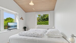 A bedroom with a bed, a TV, a lamp, and two windows with views of greenery. - "Dreng" - 250m from the sea by Interhome (Nexø)