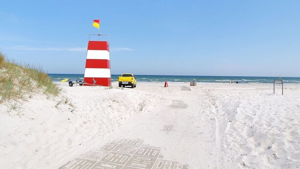 A beach with a red and white striped lighthouse, a yellow vehicle, and footprints leading to the water. - "Dreng" - 250m from the sea by Interhome (Nexø)
