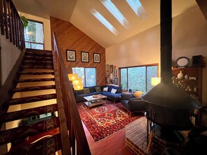 A spacious living area with a staircase, a fireplace, and large windows.