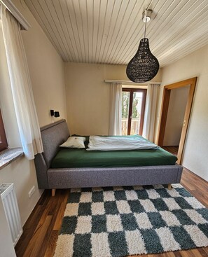Un dormitorio con un rug con diseño de cuadros, una cama con ropa de cama verde, una lámpara colgante y una ventana con cortinas.