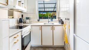 A modern kitchen with white cabinets, a stove, a coffee maker, and a window with a view of greenery.