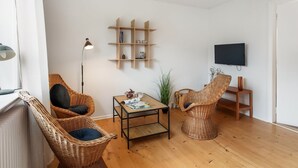 A living room with wicker furniture, a wooden coffee table, a floor lamp, a TV, and a bookshelf.