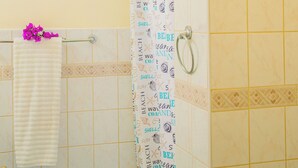 Een badkamer met een douchegordijn met tekst over het strand, een handdoekhouder met een witte handdoek, en een schilderij van een strandgezicht aan de muur.