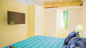Een slaapkamer met een bed, een aan de muur bevestigde televisie en een raam met gordijnen.