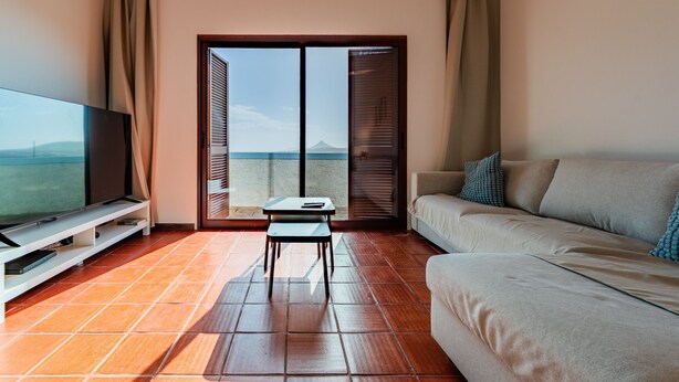 A living room with a TV, a sofa, a small table, and a sliding glass door leading to a balcony. - Sailor House - By Wehost (Porto Santo)