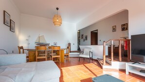 A modern living room with a sofa, a dining table, a TV, and a staircase leading to another level. - Sailor House - By Wehost (Porto Santo)