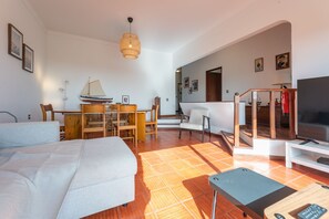 A modern living room with a sofa, a dining table, a TV, and a staircase leading to another level.