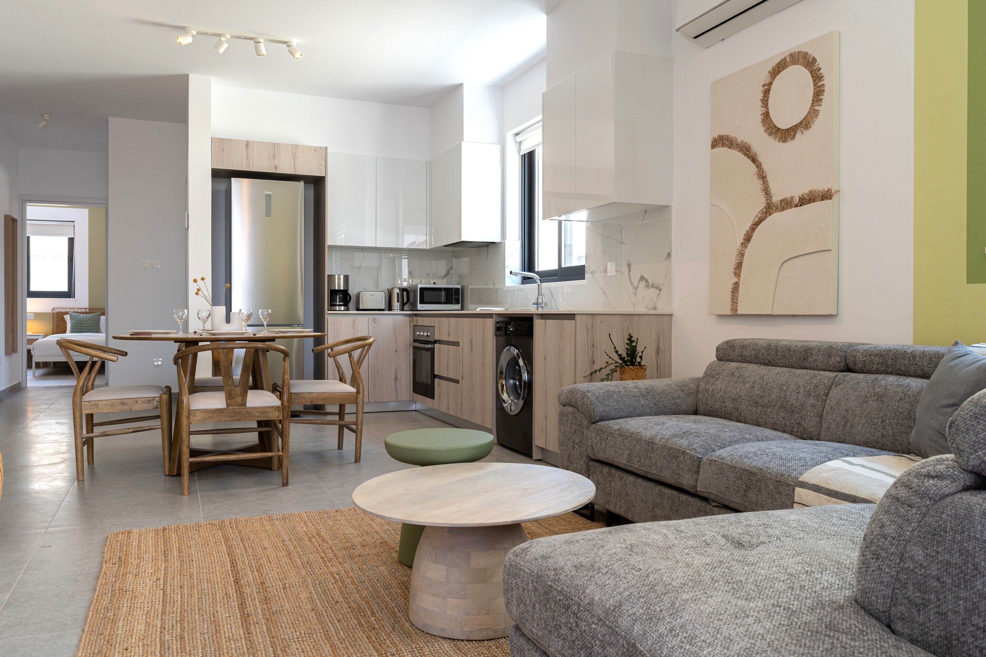 Un soggiorno moderno con un divano grigio, un tavolino rotondo e un'area pranzo con sedie e tavolo in legno.