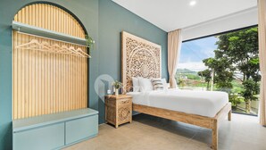 Een slaapkamer met een bed, een houten hoofdbord, een kledingkast en uitzicht op groen.