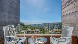 A balcony with two white wicker chairs, a small round table, and a glass barrier. - RedRock Faqra - Mountain Getaway Residences W Pool & Balconies (Bqaatouta)