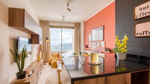 A modern kitchen with a large island, a dining area with a sofa, and a view of the city. - RedRock Faqra - Mountain Getaway Residences W Pool & Balconies (Bqaatouta)