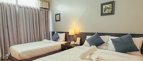Une chambre d’hôtel avec deux lits, une table de chevet, une lampe et une fenêtre avec des rideaux.