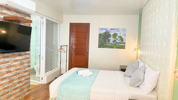 Habitación de hotel con una cama, un televisor, un cuadro y una puerta.