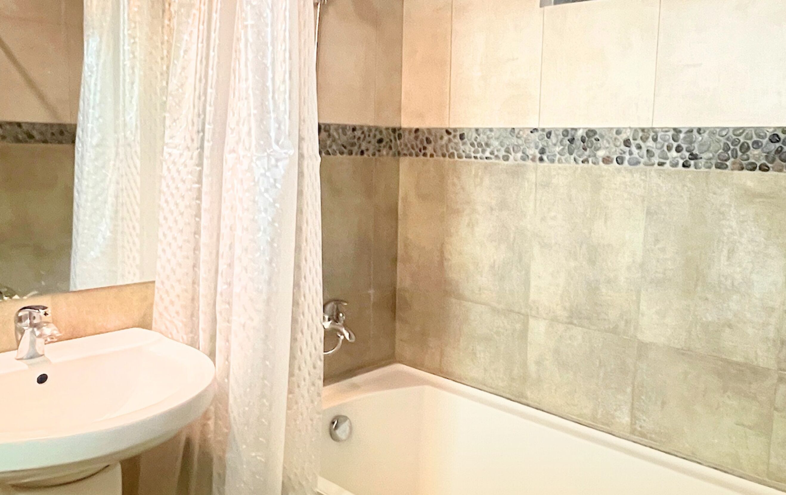 A bathroom with a sink, a bathtub, and a shower curtain.