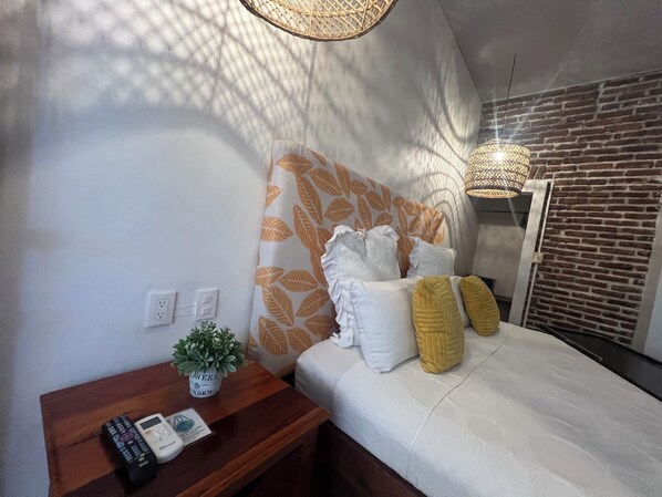 A bedroom with a bed, a bedside table with a plant, a lamp, and a brick wall. - EJECUTIVO CESAR MARISCOS (Tela)