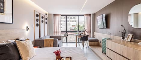 Habitación de hotel moderna con cama, escritorio, zona de comedor y vistas a la ciudad.
