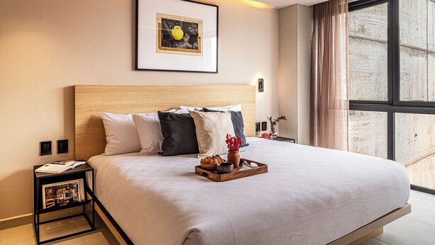 A hotel room with a large bed, a framed picture on the wall, a nightstand, and a window with curtains. - Kukun Tonalá 121 Roma  (Mexico City)