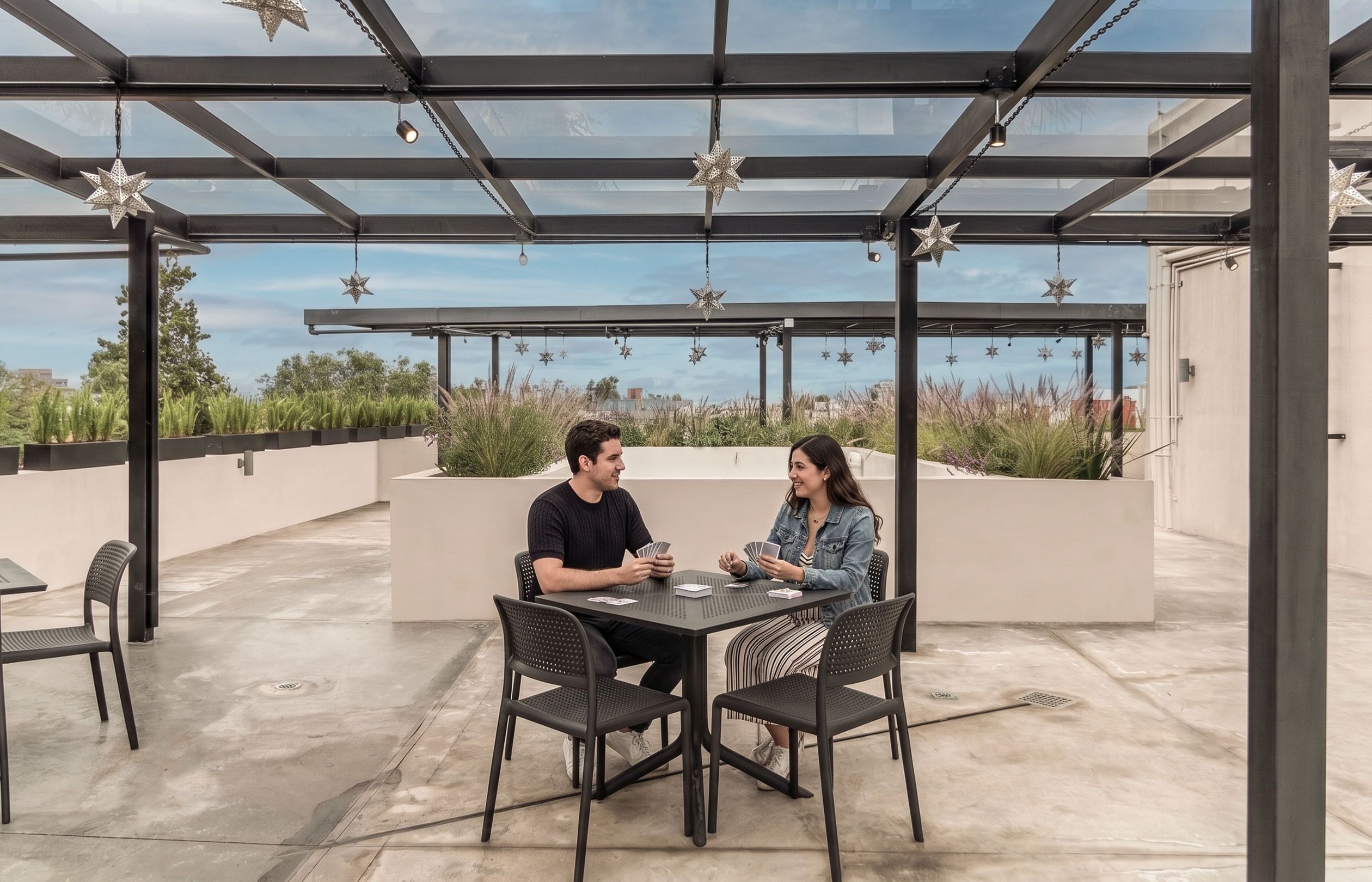 A covered outdoor seating area with a table and chairs, star-shaped hanging decorations, and a view of the sky and distant buildings.