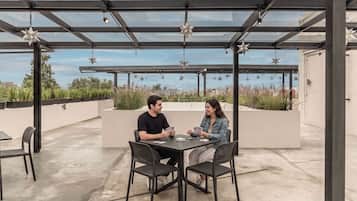 A covered outdoor seating area with a table and chairs, star-shaped hanging decorations, and a view of the sky and distant buildings.