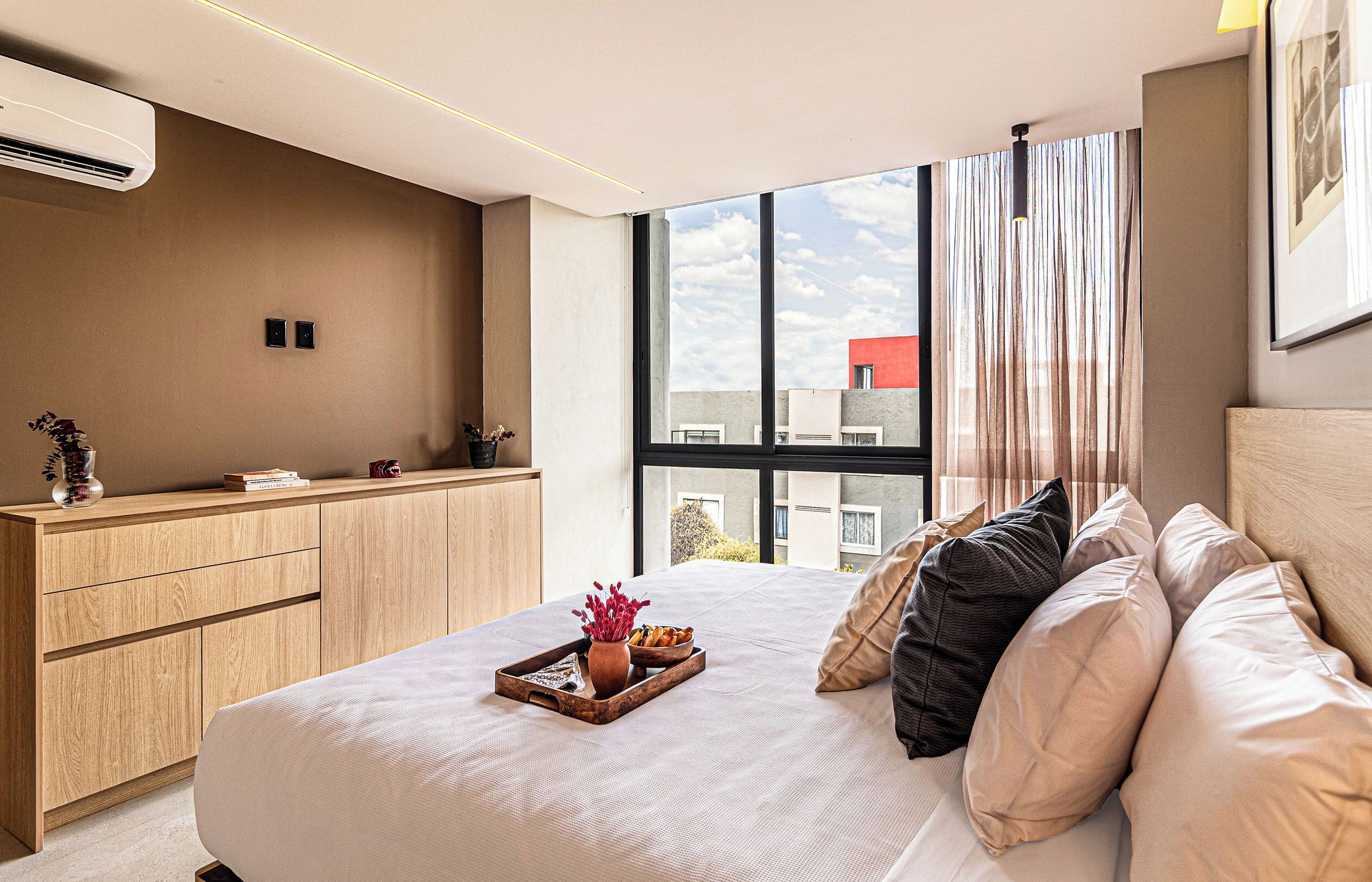 Een moderne slaapkamer met een groot bed, een houten garderobe, een raam met gordijnen en een airconditioning.