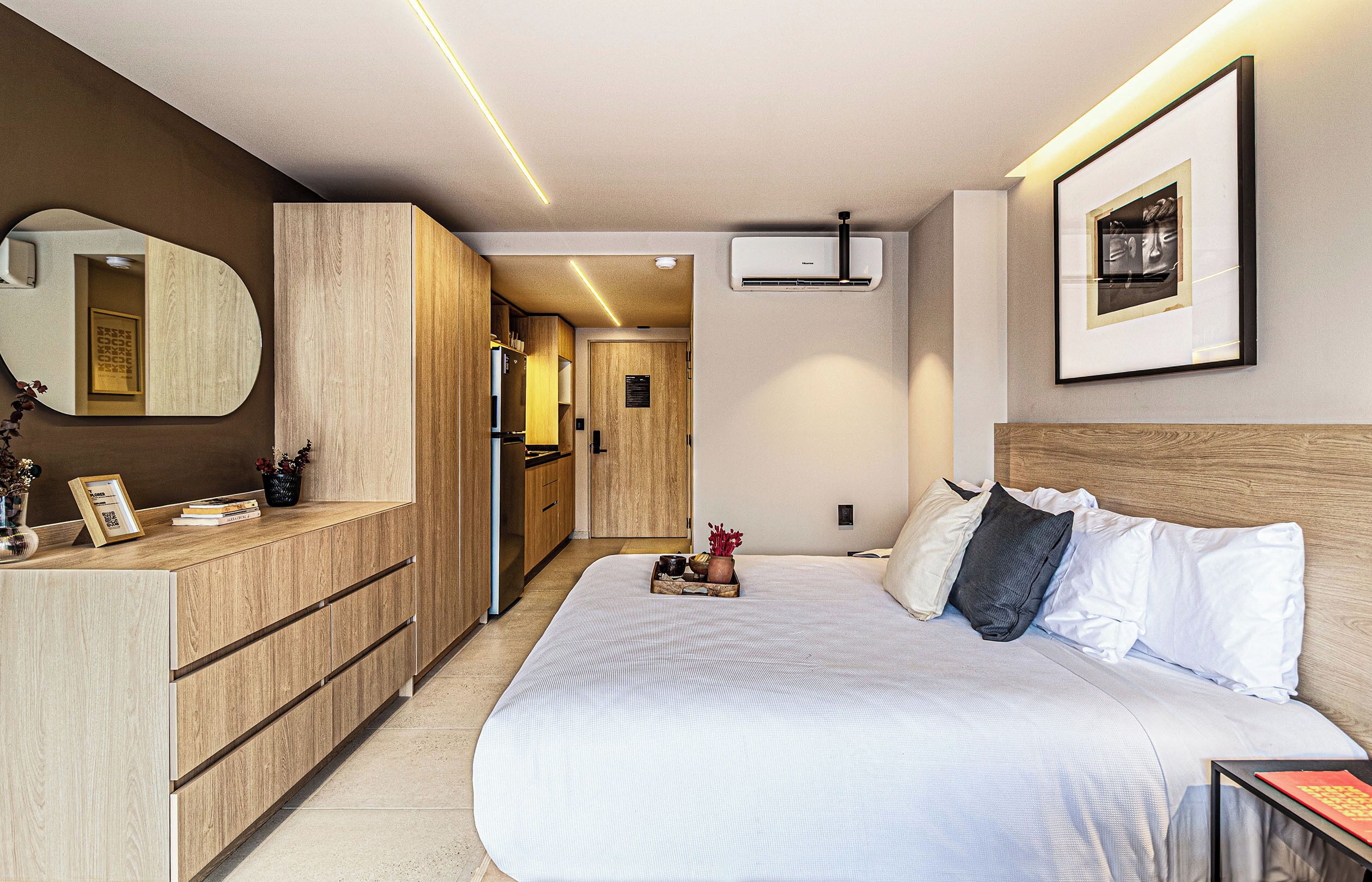 Una habitación de hotel moderna con una cama grande, un armario de madera y una pequeña kitchenette.
