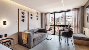 A modern living room with a sofa, a dining table with chairs, and a large window offering a city view.