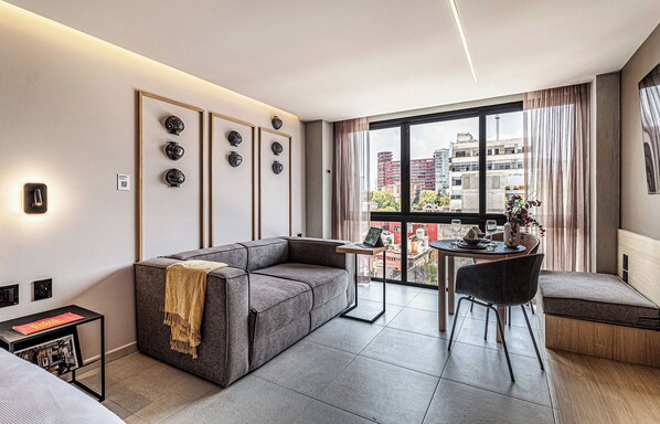 Una sala de estar moderna con un sofá, una mesa de comedor con sillas y un amplio ventanal con vista a la ciudad.