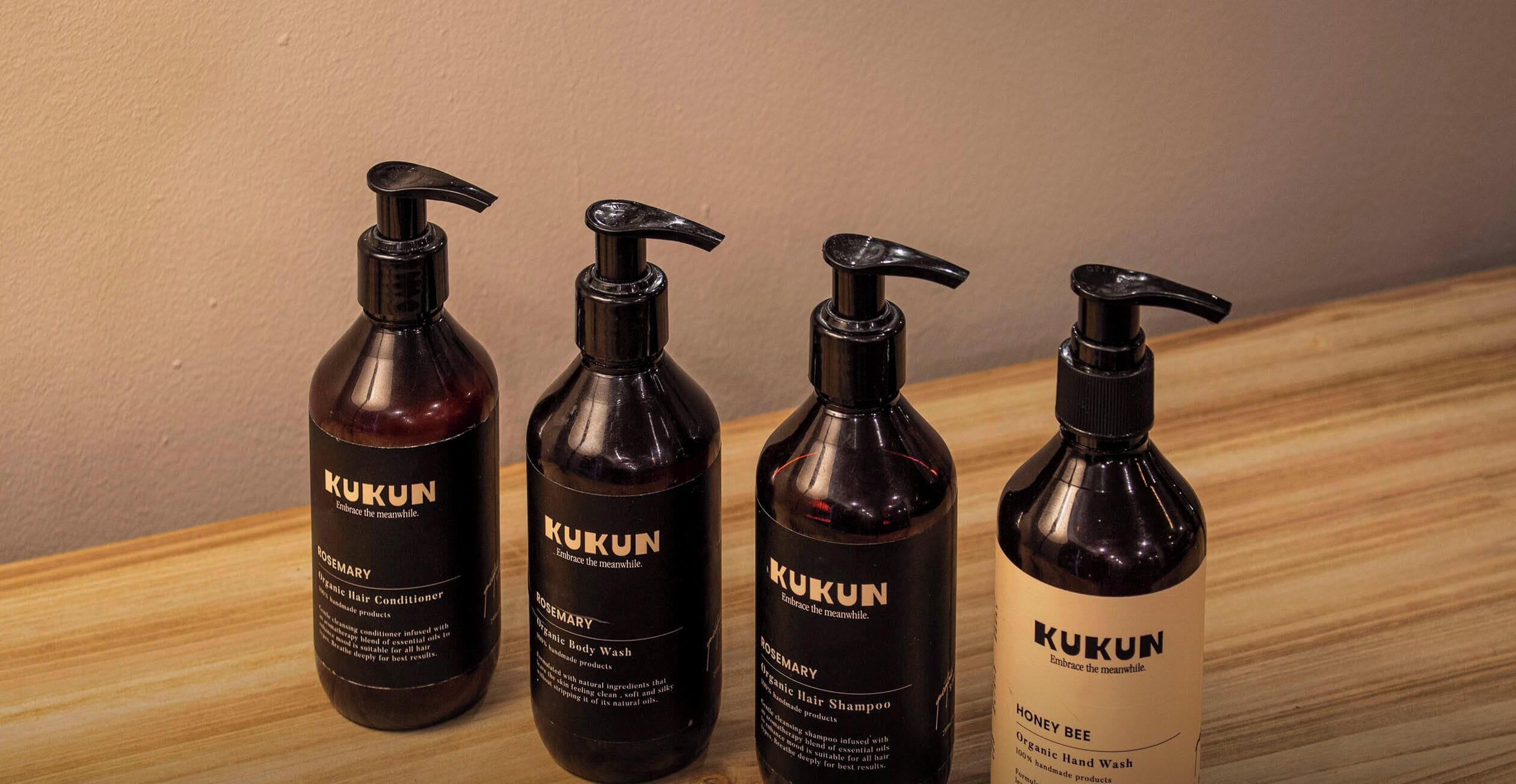 Four bottles of Kukun hair care products on a wooden surface.