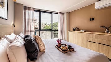Une chambre d’hôtel avec un lit, une table de chevet sur laquelle se trouve un plateau de nourriture, un vase rempli de fleurs et une vue sur les bâtiments par la fenêtre.