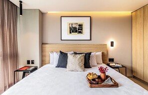 Una habitación de hotel impecable con una cama grande, una mesita de noche con un libro, un cuadro en la pared y una lámpara en el buró.