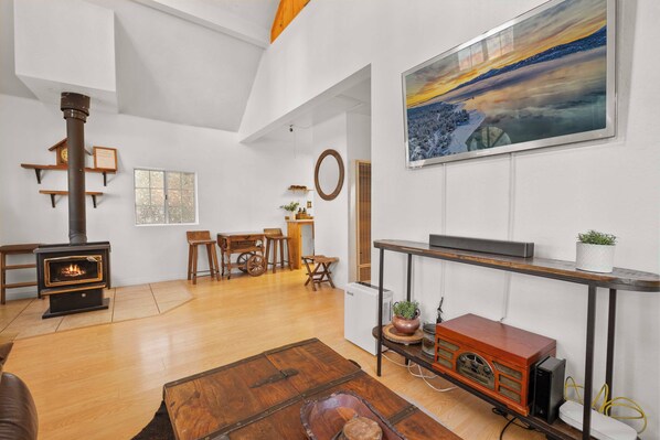 A living room with a fireplace, wooden furniture, a painting, and a television. - Moonridge Haus (Big Bear Lake)