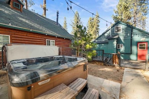A hot tub in front of a wooden cabin with a green roof and a red door. - Moonridge Haus (Big Bear Lake)