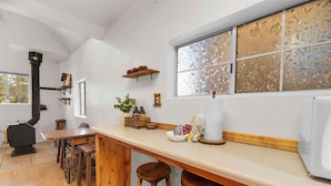 A kitchen with a wooden table, stools, a stove, and a window with frosted glass.