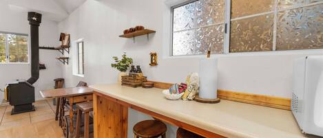 A kitchen with a wooden table, stools, a stove, and a window with frosted glass.
