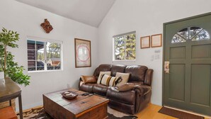 A living room with a brown leather sofa, a wooden coffee table, a large window, and a green door.