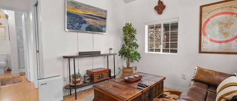 A living room with a wooden coffee table, a brown leather sofa, a large painting, a globe, and a potted plant.