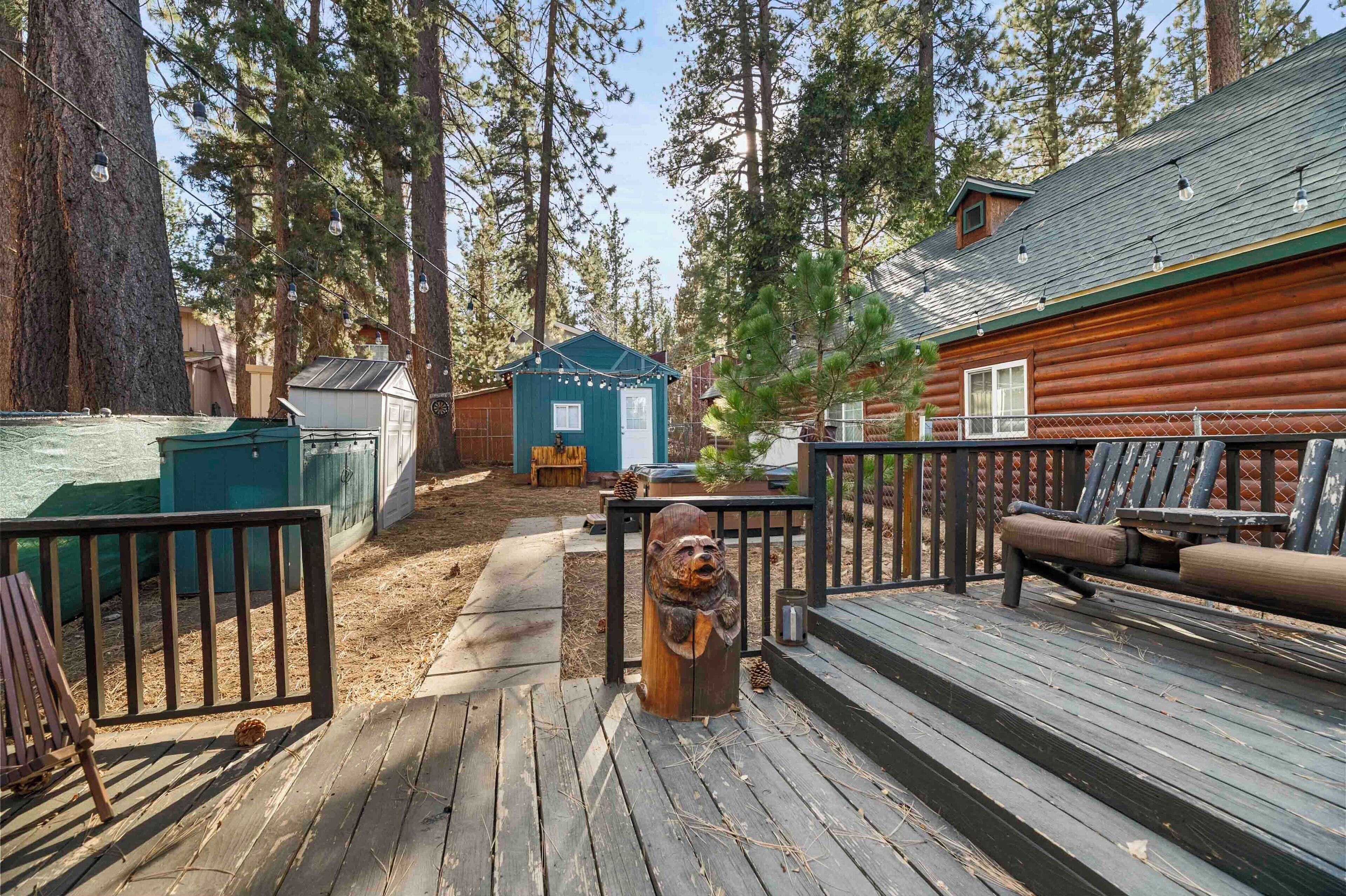 A wooden deck with a bench, a small shed, and a cabin in a forested area.