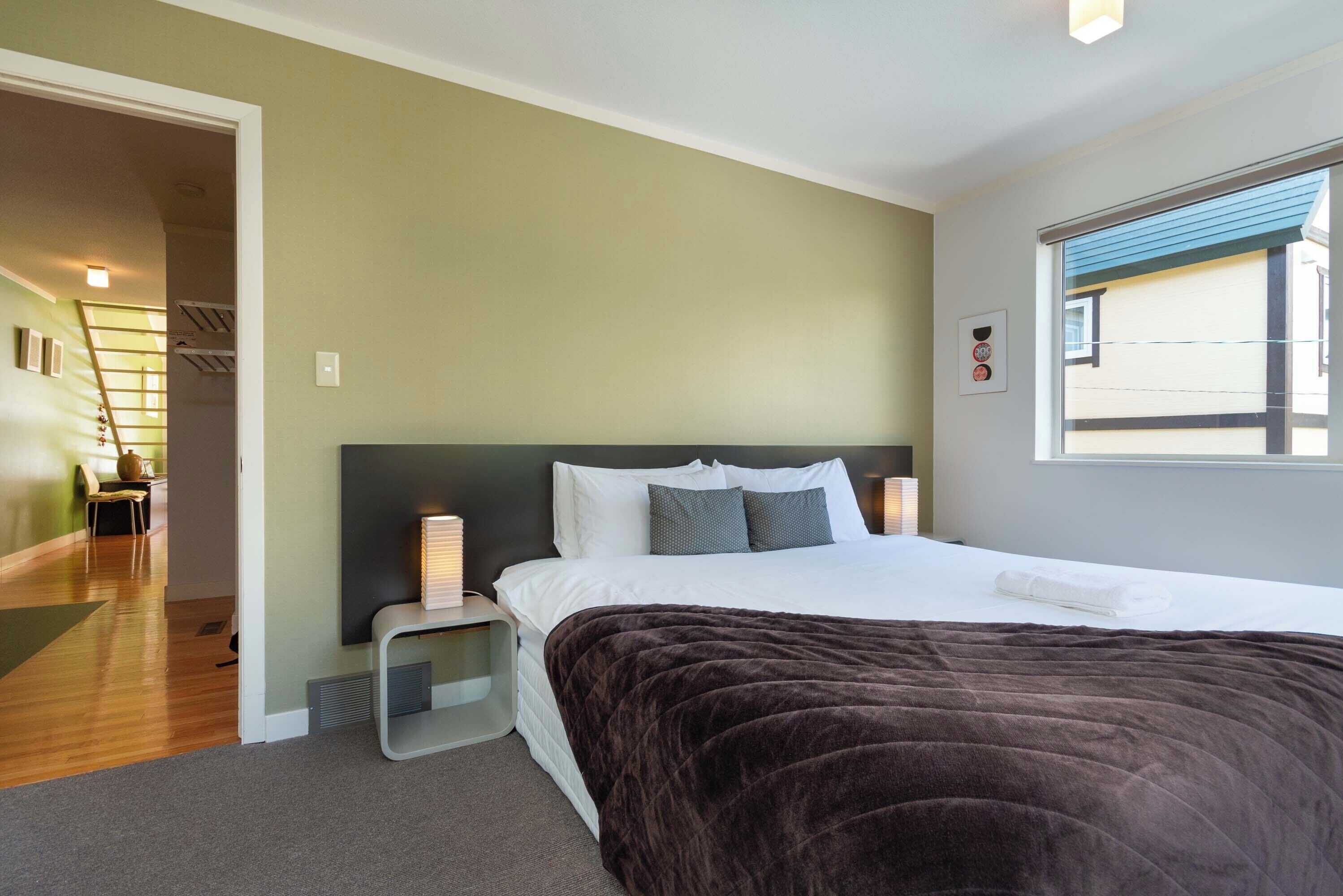 A bedroom with a large bed, a nightstand, a chair, and a window.