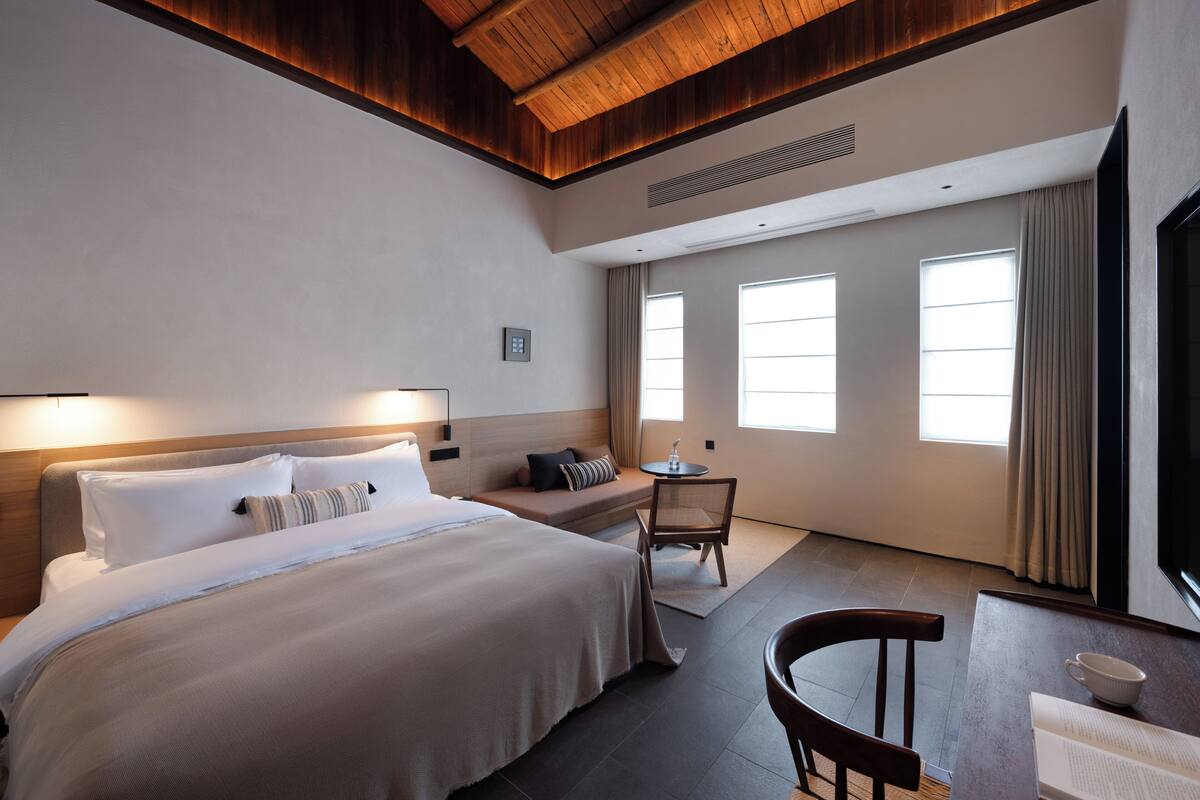 A hotel room with a large bed, a desk, a chair, a TV, and a window with curtains.