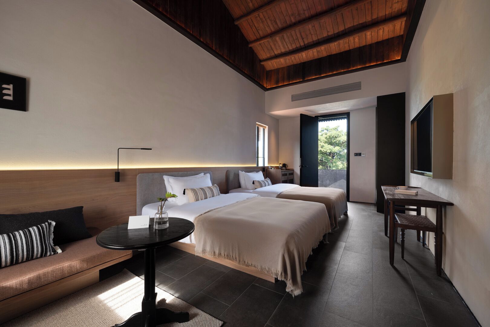 A modern hotel room with two beds, a sofa, a small table, and a TV.