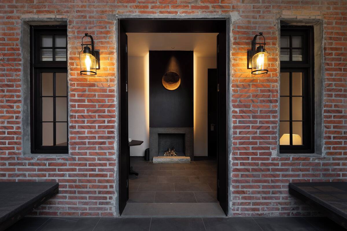 A brick building with a fireplace, two lit wall sconces, and a door leading to a hallway.
